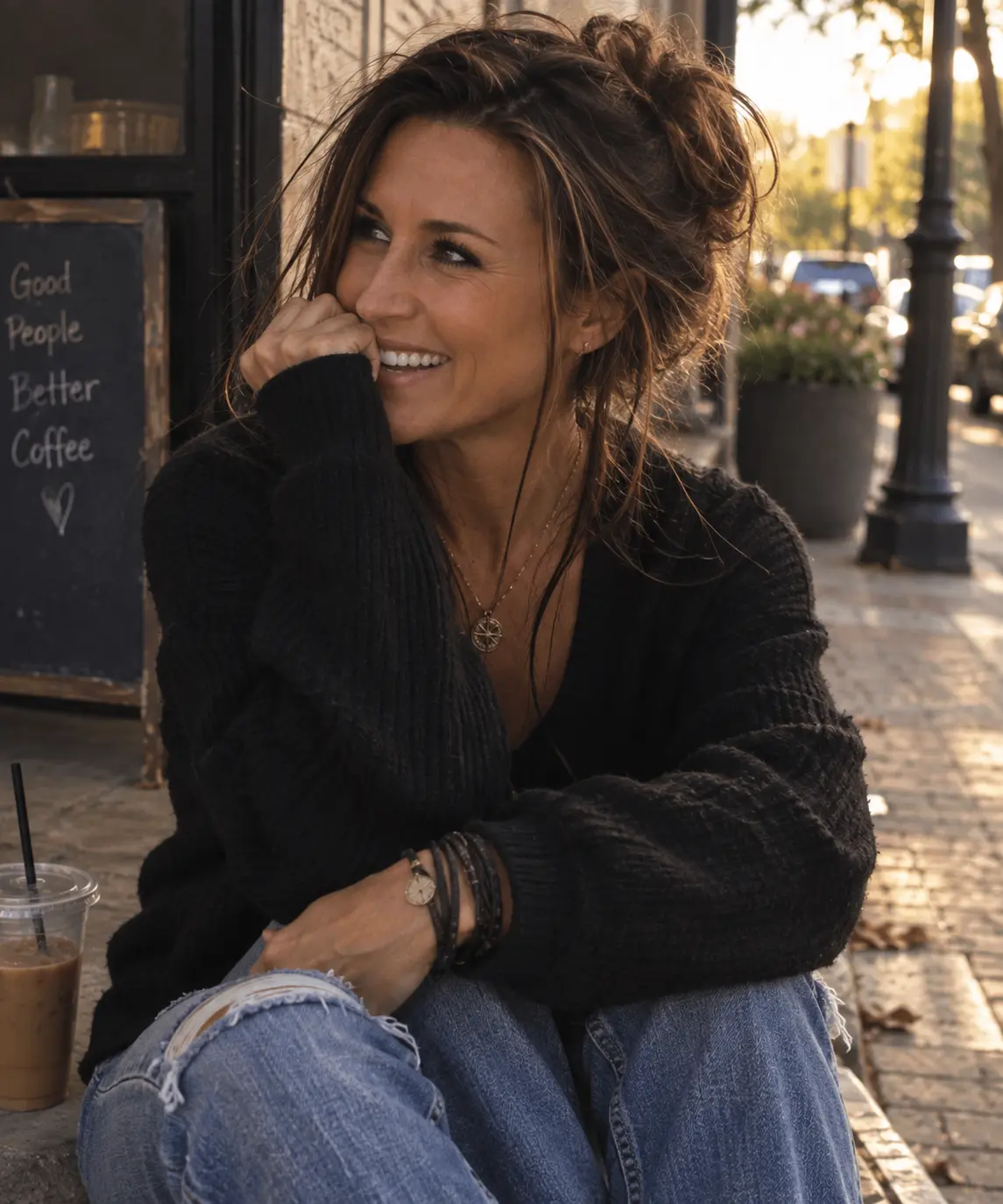 Lore Lassen laughing on a sunlit kerb outside a coffee shop, iced coffee beside her